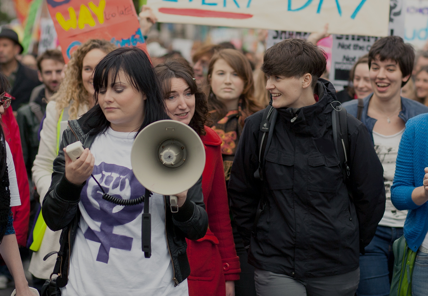 Image of protesters or activists led by a young woman with a megaphone