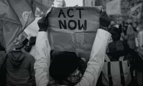 Black and white image of person holding up a sign that says ACT NOW
