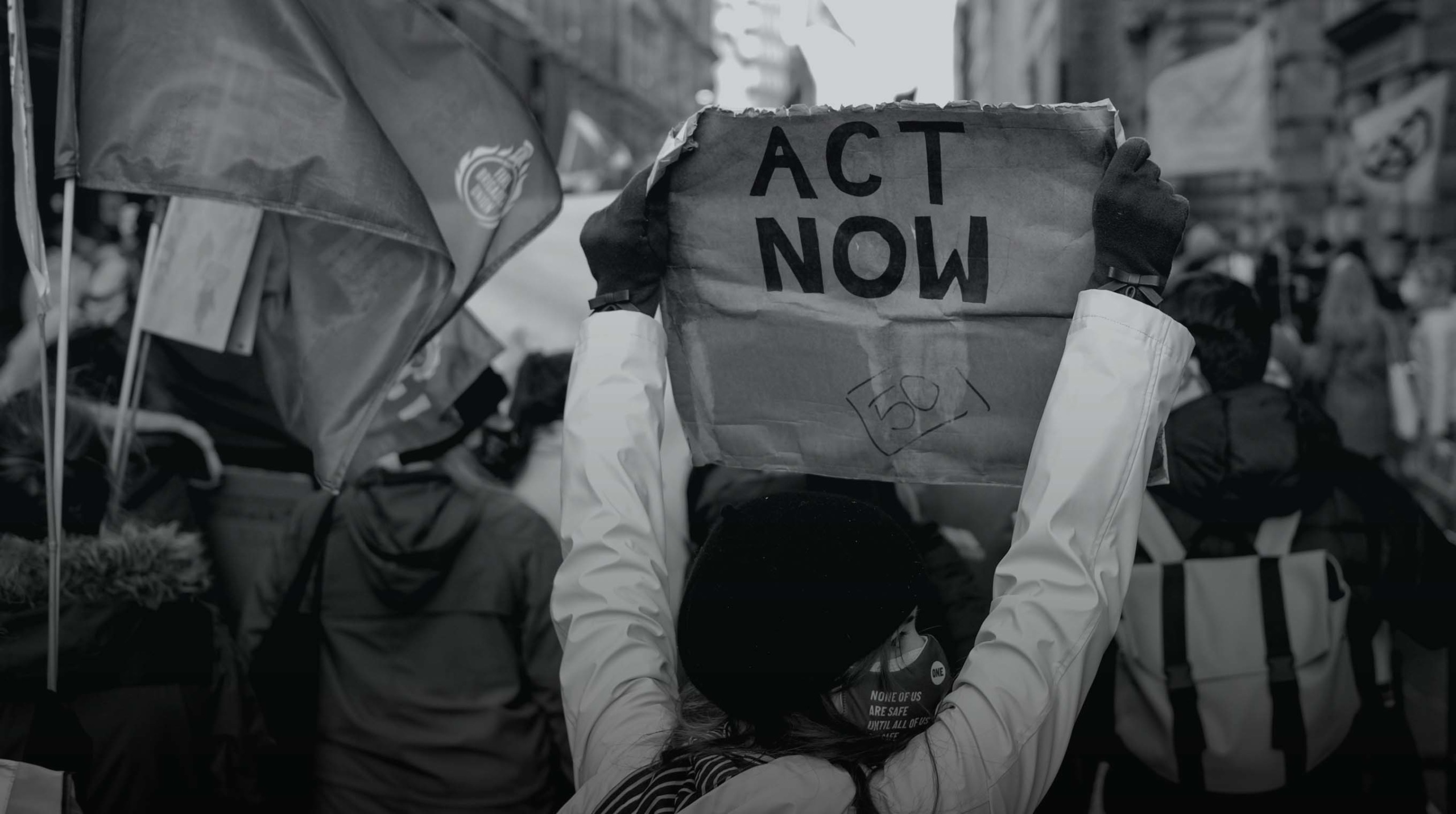 Black and white image of a person holding up a sign that says ACT NOW