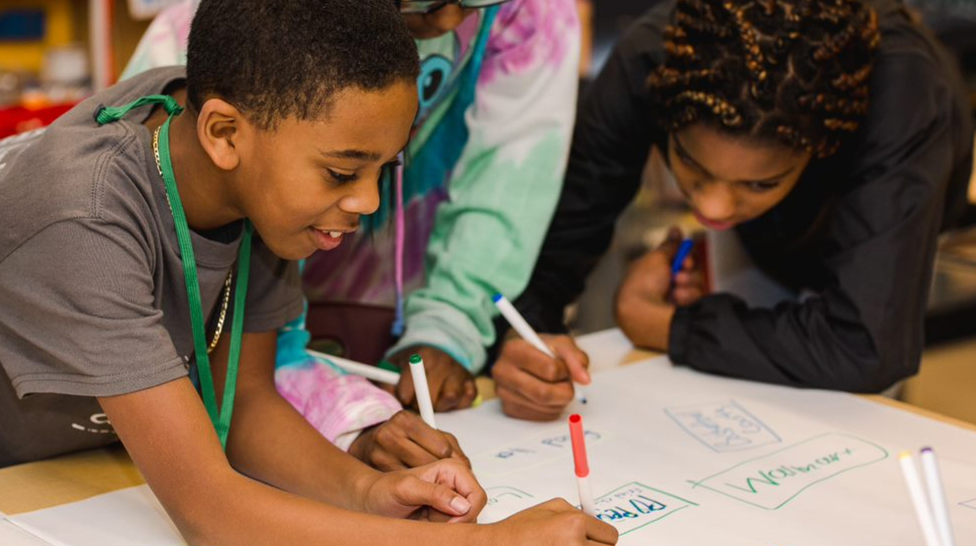 A Black student draws on paper in a classroom with his classmates