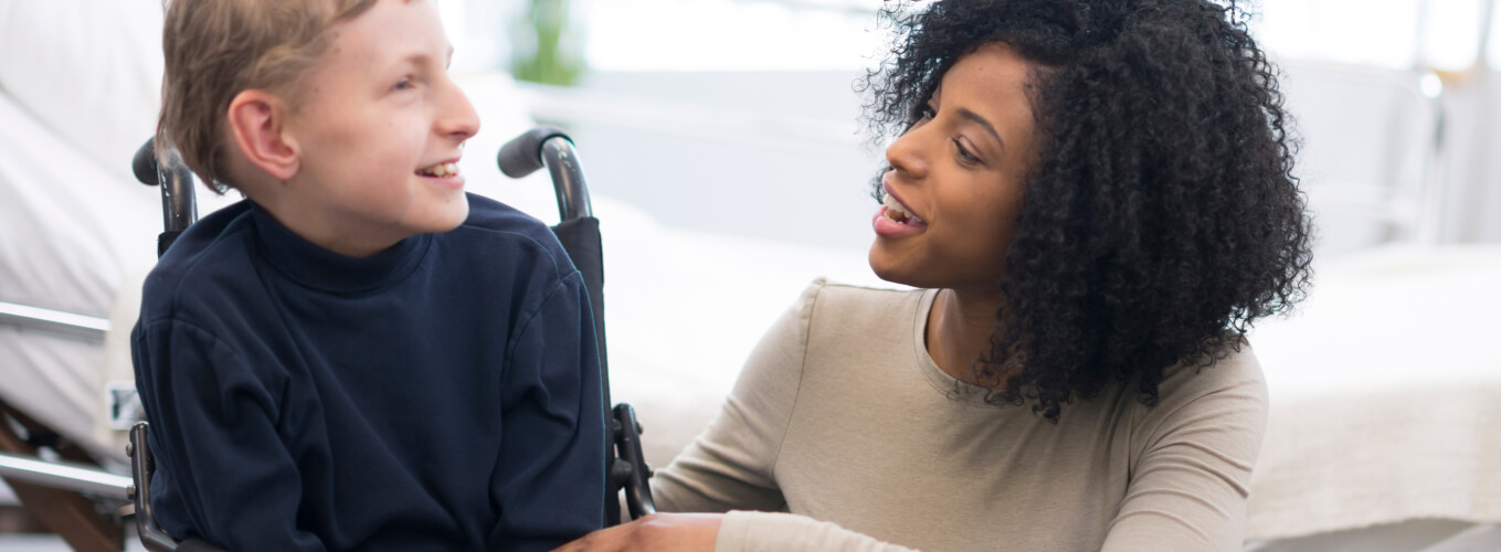 A boy in a wheel chair smiling at his female caregiver