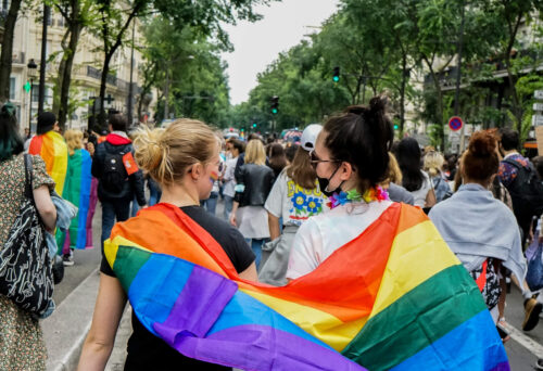 Two individuals at a parade with a pride flag draped over their shoulders