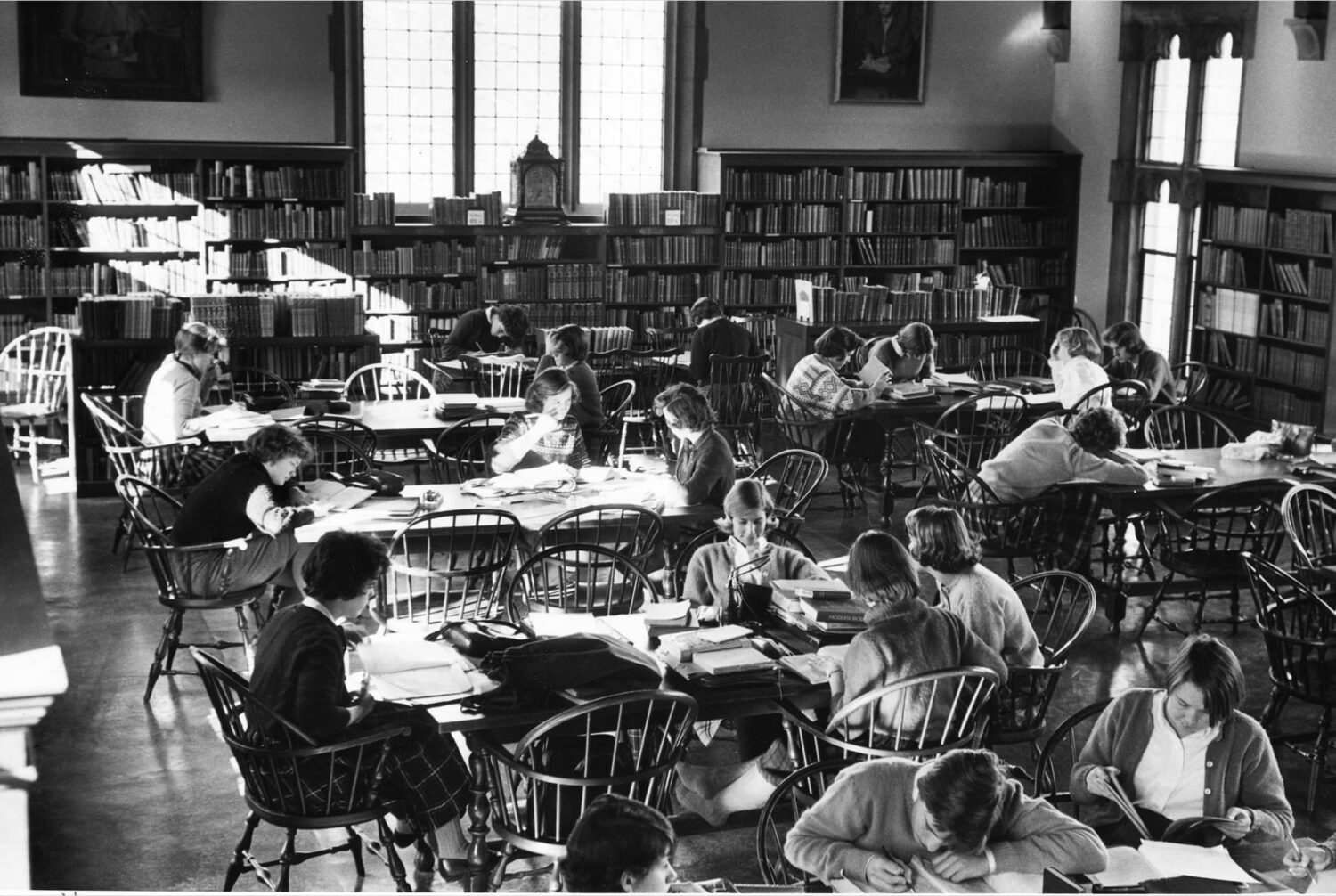 Historic black and white photo of a full library: women sit at wooden tables and study.